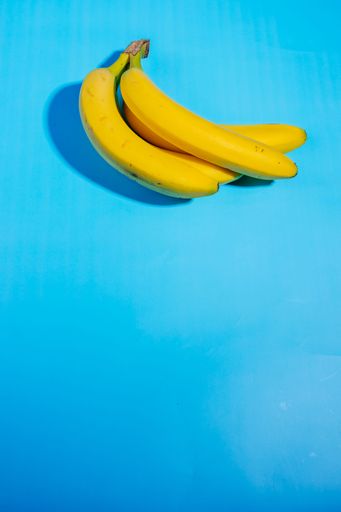 A vertical closeup shot of yellow bananas isolated on a light blue background