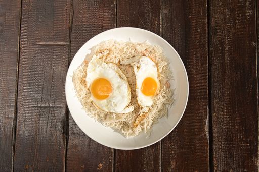 A top view shot of a rice dish with fried eggs on it, served on a white plate on a wooden table