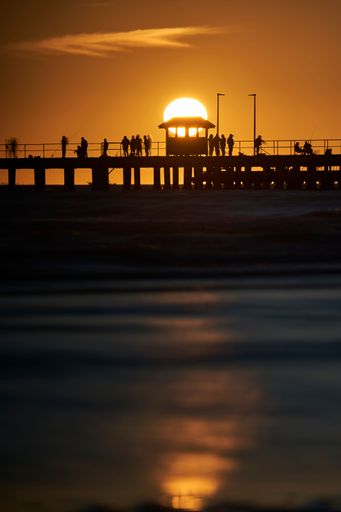 A vertical shot of a bridge over a lake at the Melbourne Pier during an orange sunset