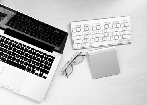 A high angle shot of a work desk with a laptop, glasses and a notepad