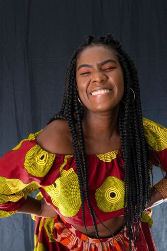 Afro-Brazilian woman smiling at camera against black background. She wears African-style clothes.