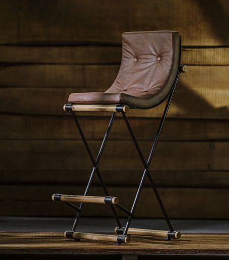 A wooden stool with a leather cushion and metal legs in a studio
