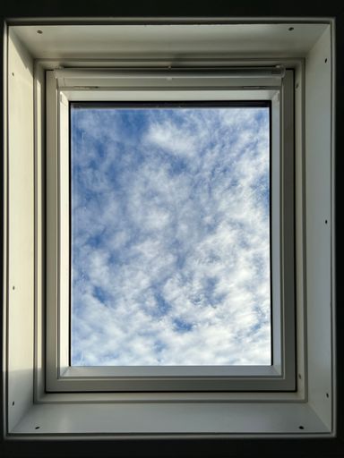 A vertical shot of view of the blue sky with windy clouds through white aluminium window on a sunny day
