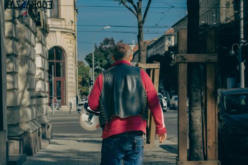 A man from behind holding a helmet and walking on the streeets of Budapest's inner city