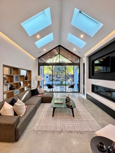 A modern interior room with a table on carpet, book shelves, glass ceiling and glass balcony