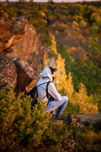 A vertical shot of a young man with a mask sitting on hill and looking to the autumn forest