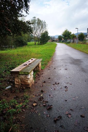 A vertical shot of a bench on a trekking route among green plains to Cubia river in Grado Asturias