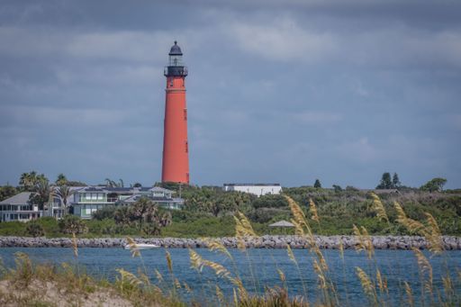 A beautiful scene of a red lighthouse near the body of water on a cloudy day