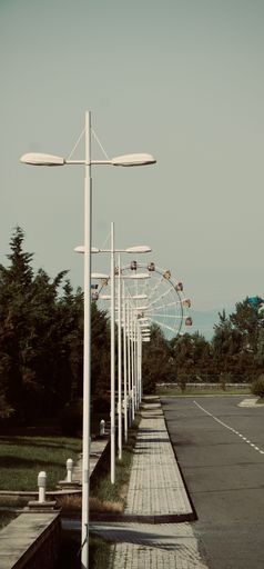 A vertical shot of street lamps with a ferris wheel in the background