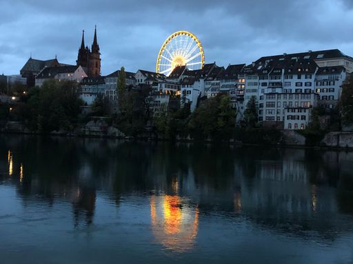 An evening at the Basel Fall fair with a Ferris wheel. It is a symbol of the fall fair. Beautiful colors are reflected in the Rhine.