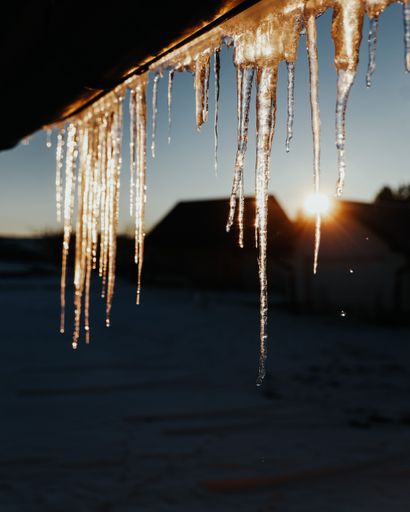 A selective focus of icicles during cold winter with houses and the sun on the background