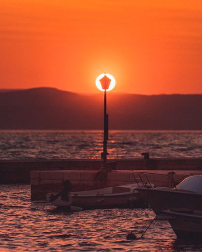A vertical image of a street light in the middle with boast below it during golden hour