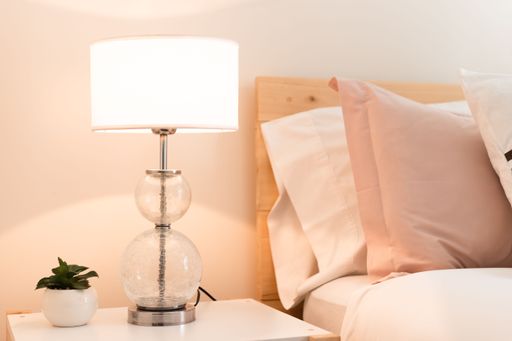 A beautiful lit lamp with a small plant on a nightstand next to the bed