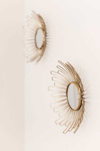 A white wall with two beautiful round gold sun mirrors