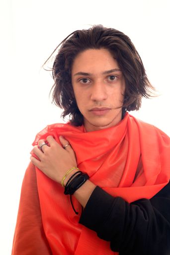 Young man with red transparent fabric over his shoulder against white background. Studio photography. Salvador, Brazil.