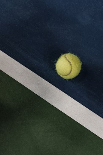 A vertical closeup shot of a tennis ball in a green and blue tennis field with a white line - great for mobile tennis related articles