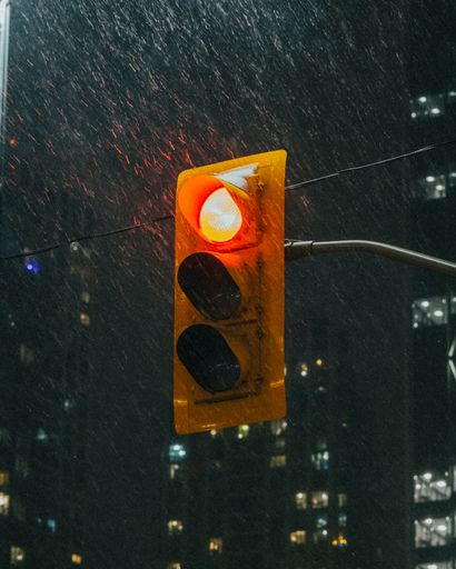 A red stoplight glowing in the pouring rain at night