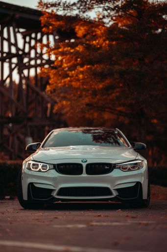 Front view of a modern white BMW M4 on the street during an autumn sunset. Luxury sports car