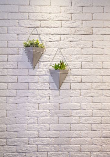 A vertical shot of two decorative triangular flowerpots suspended from a white brick wall