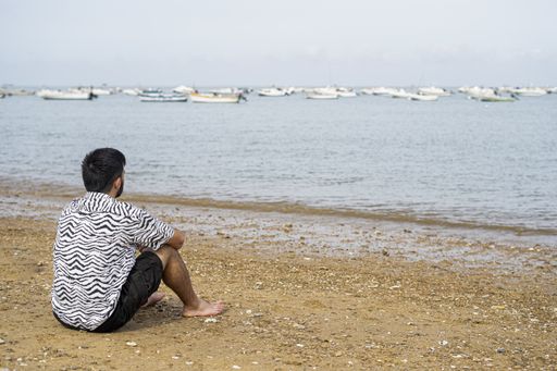 A Hispanic man sitting on the shore while enjoying the view of the sea on a sunny day