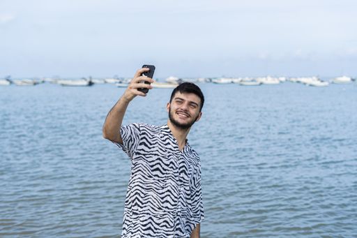 A Hispanic man taking selfies at a beach