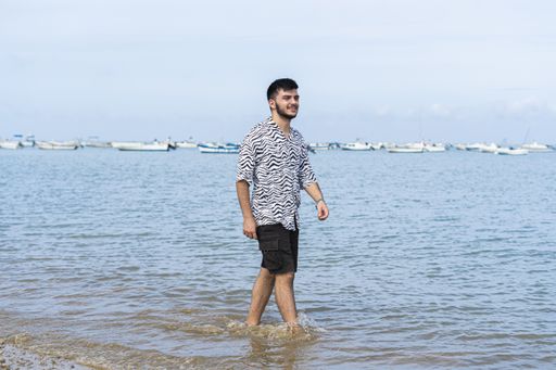 A Hispanic man wearing protective mask while wading barefooted at a beach on a sunny day