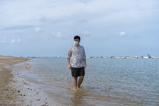 A Hispanic man wearing protective mask while wading barefooted at a beach on a sunny day