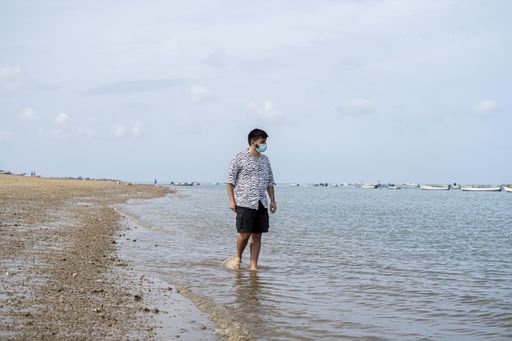 A Hispanic man wearing protective mask while wading barefooted at a beach on a sunny day