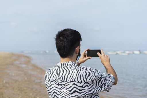 A Hispanic man taking photos of the sea on his smartphone on a sunny day