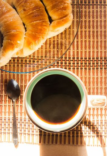 A vertical shot of a morning cup of coffee and a plate of croissants