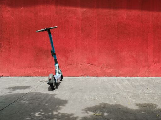 A closeup of an electric scooter parked against a bright red wall in the streets