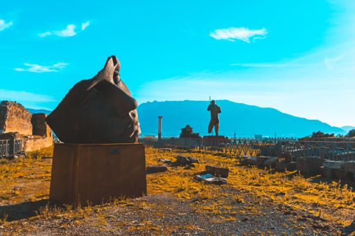A memorial with sculptures surrounded by greenery with mountains on the background under sunlight
