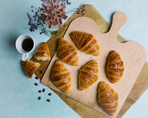 A top view of homebaked croissants on a wooden board displayed  with a cup of coffee and coffee beans