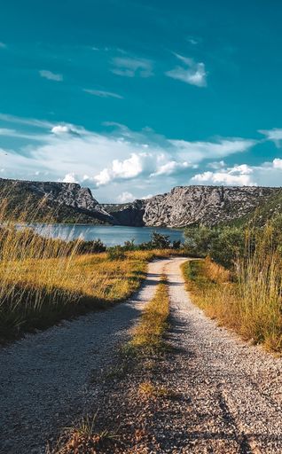 A vertical shot of a path leading to a beautiful lake and big rocky mountains under a blue sky